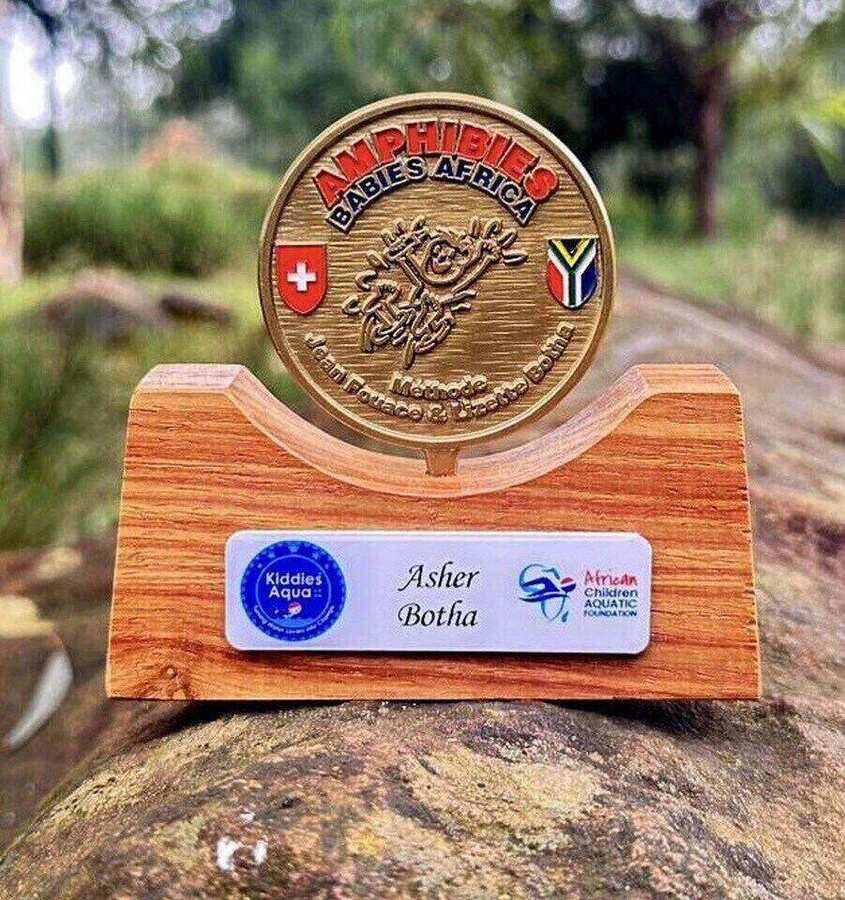 Personalised Amphibies Babies Africa gold-mounted coin awarded to a qualifying KASA baby — mounted on a wooden stand with the child's name plaque