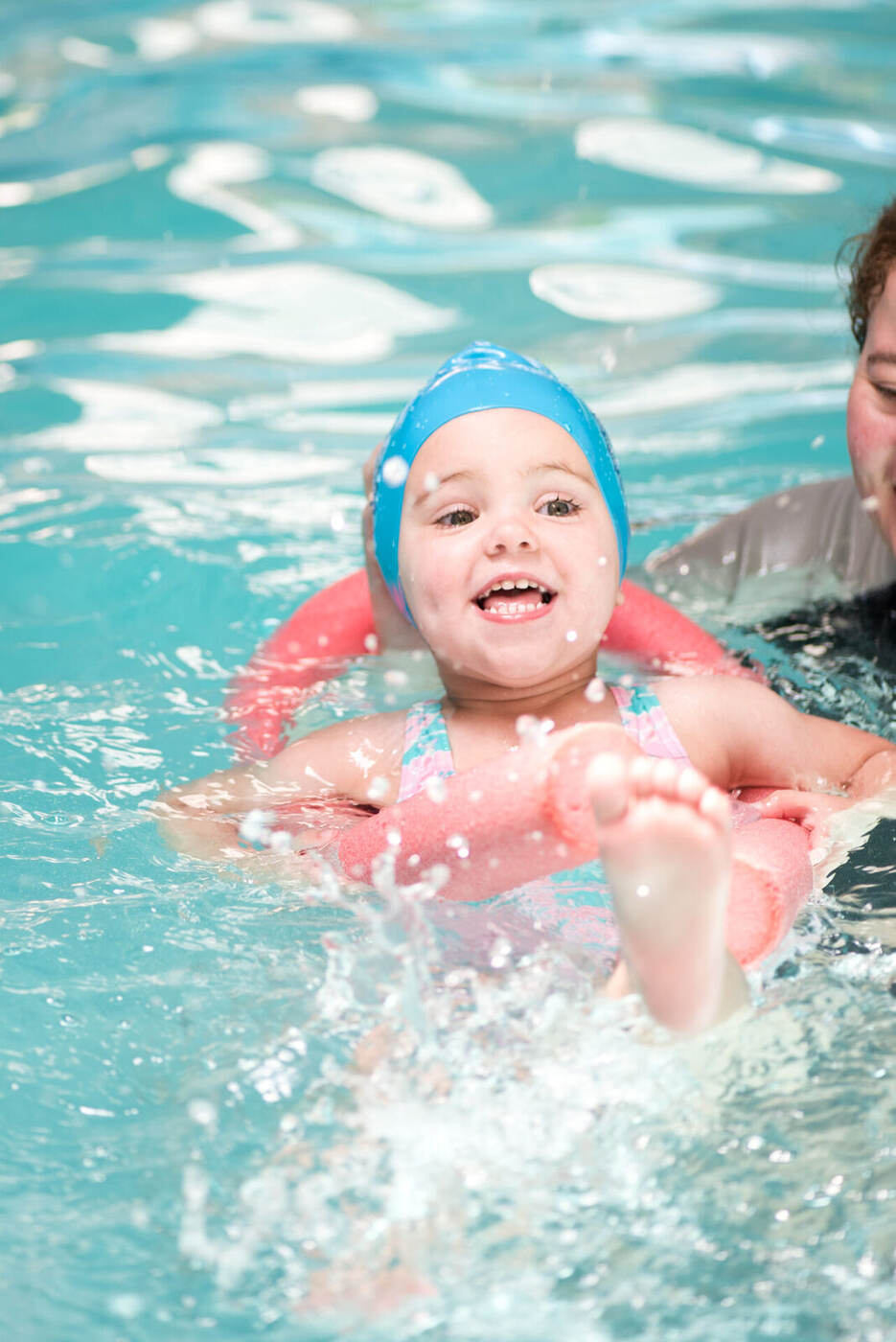 Smiling young child holding a pool noodle during a Kiddies Aqua class